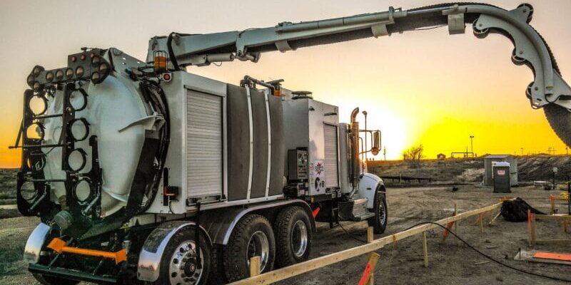 White X-Vac hydro-excavation truck with articulated boom extended at sunset on a construction site